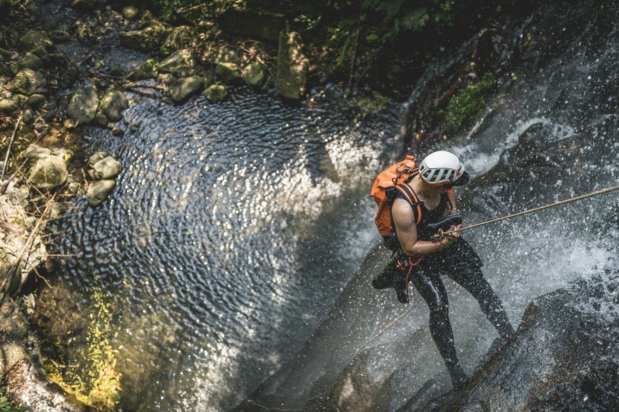 A canyoning guest in a helmet abseiling down a waterfall
