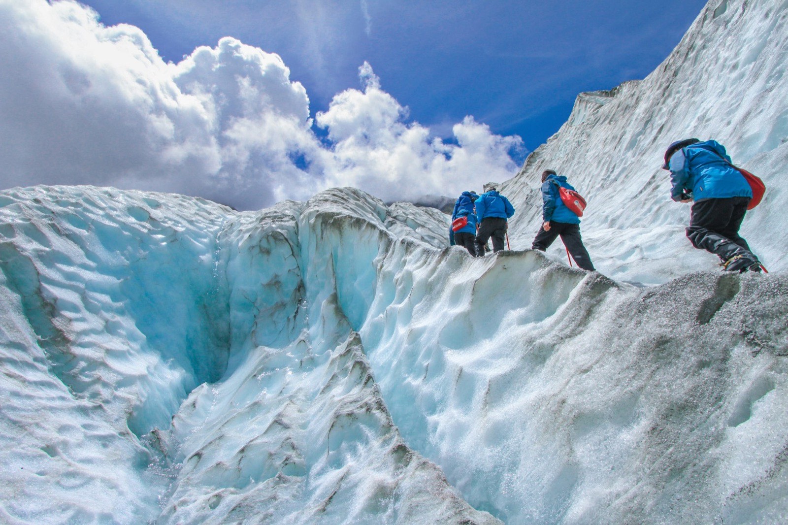 Four climbers roped together crossing blue glacier ice under a bright sky