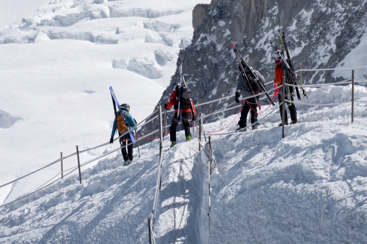 A roped party of mountaineers walking a snowy ridge path in a line